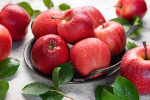 Fresh red apples resting on rustic metal plate with green leaves, a Food & Drink Photo by Olena Rudo