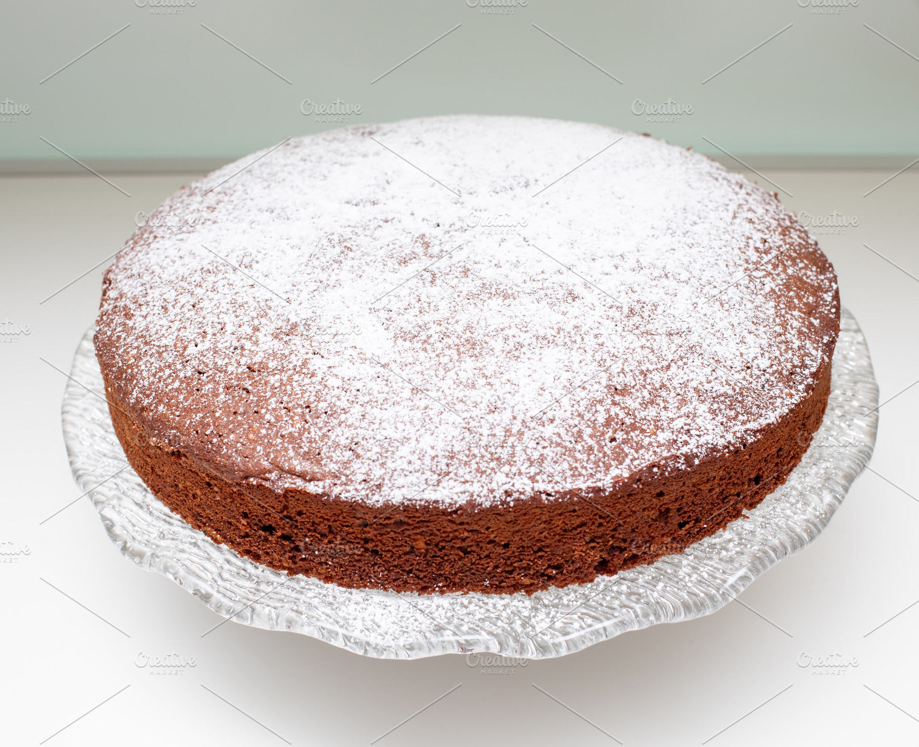 Round caprese cake with icing sugar on glass cake stand, a Food & Drink Photo by Antonio Gravante Market