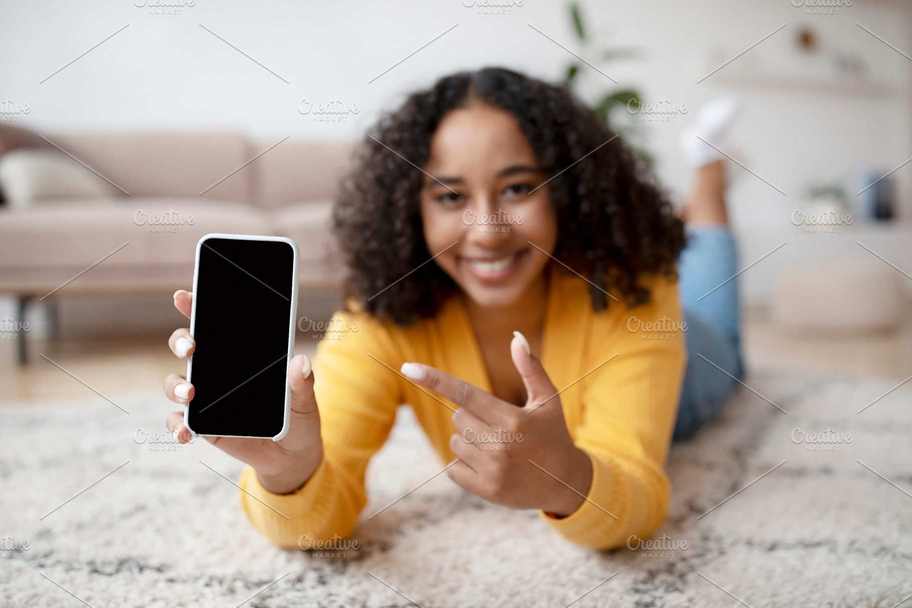 Happy young African American woman pointing at smartphone with empty screen, ly, a Photo by Prostock-Studio
