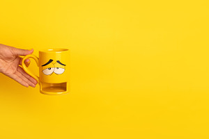 Hand in yellow sweater holding a yellow mug with a sleepy carto, a Food & Drink Photo by Ales Munt