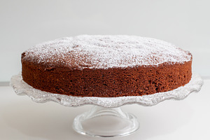 Delicious caprese cake resting on elegant glass cake stand, sprinkled with powd, a Food & Drink Photo by Antonio Gravante Market
