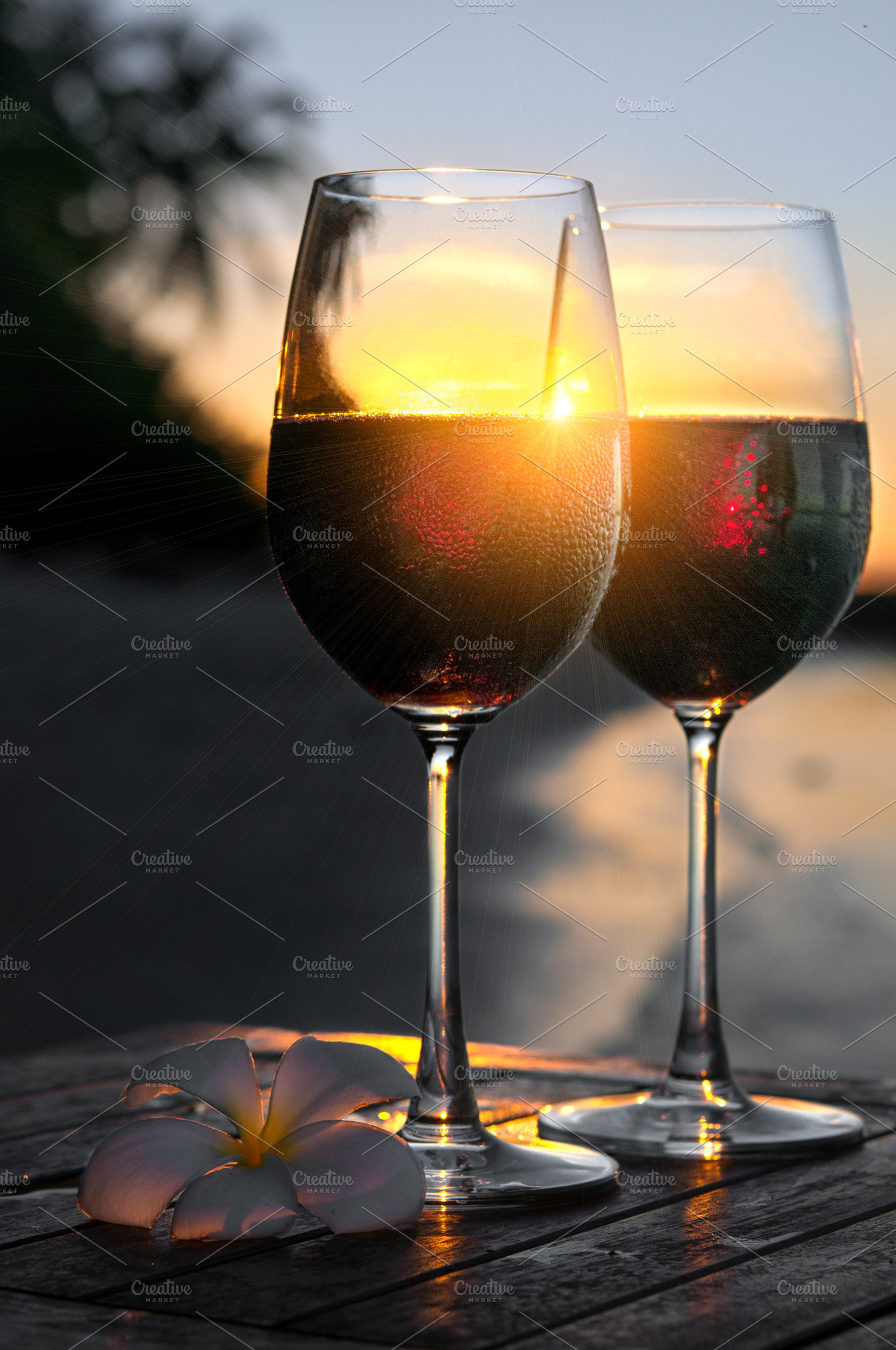 Romantic beach scene: two glasses of red wine at sunset near water, a Photo by Edgieus