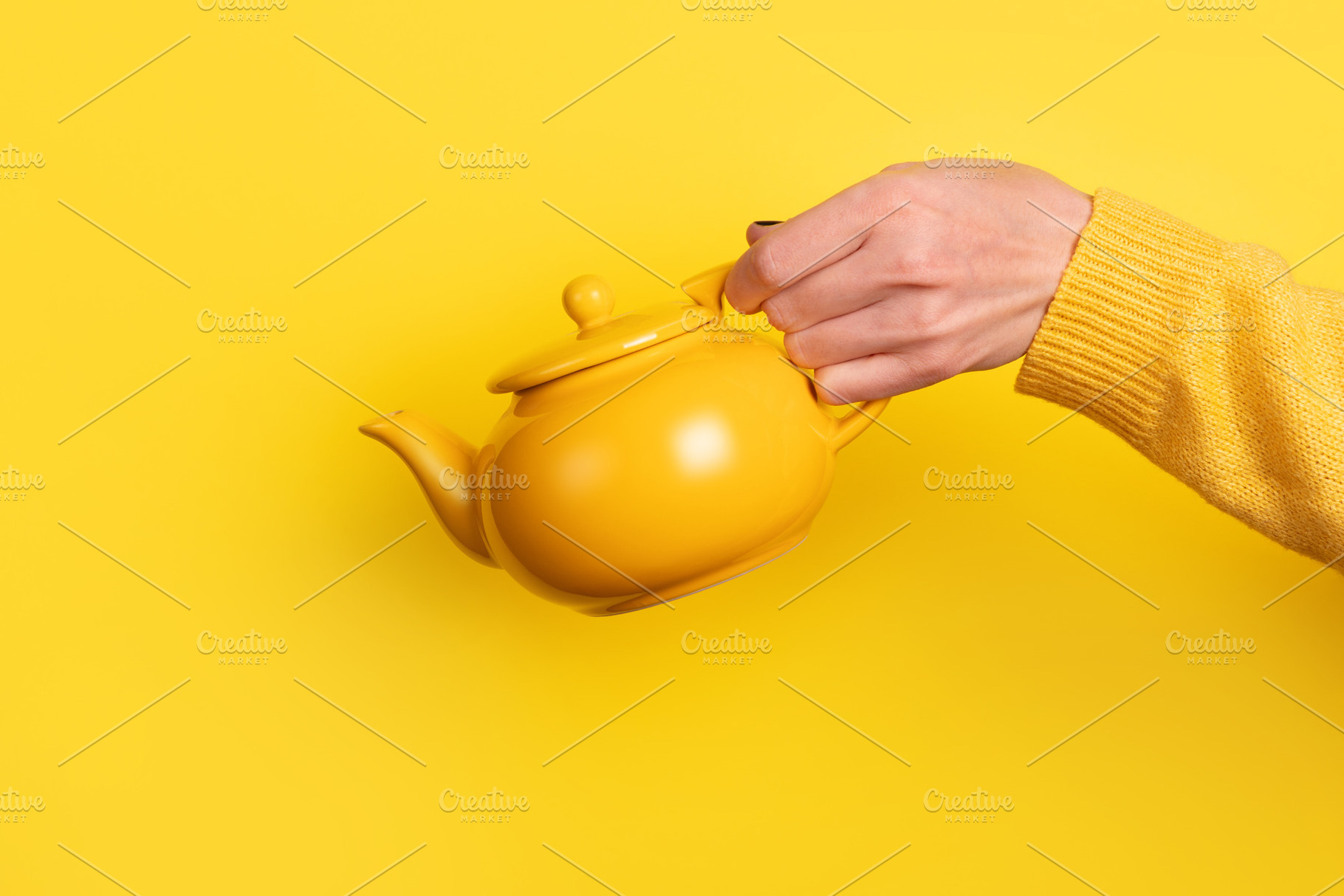A hand in a yellow sweater holds a yellow teapot against a vibra, a Food & Drink Photo by Ales Munt