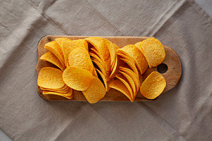 Bacon flavoured potato chips on a wooden board, top view., a Food & Drink Photo by LiudmylaChuhunova