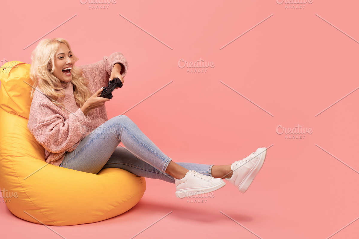 Joyful woman playing video games with joystick, sitting on beanbag chair over p, a Photo by Prostock-Studio (Photo 1 of 2)