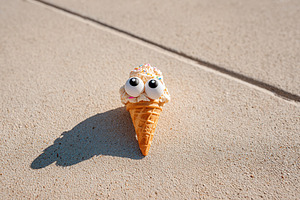 Ice cream cone with googly eyes rests on a sunny surface casting a whimsical sh, a Food & Drink Photo by AlyaAnd