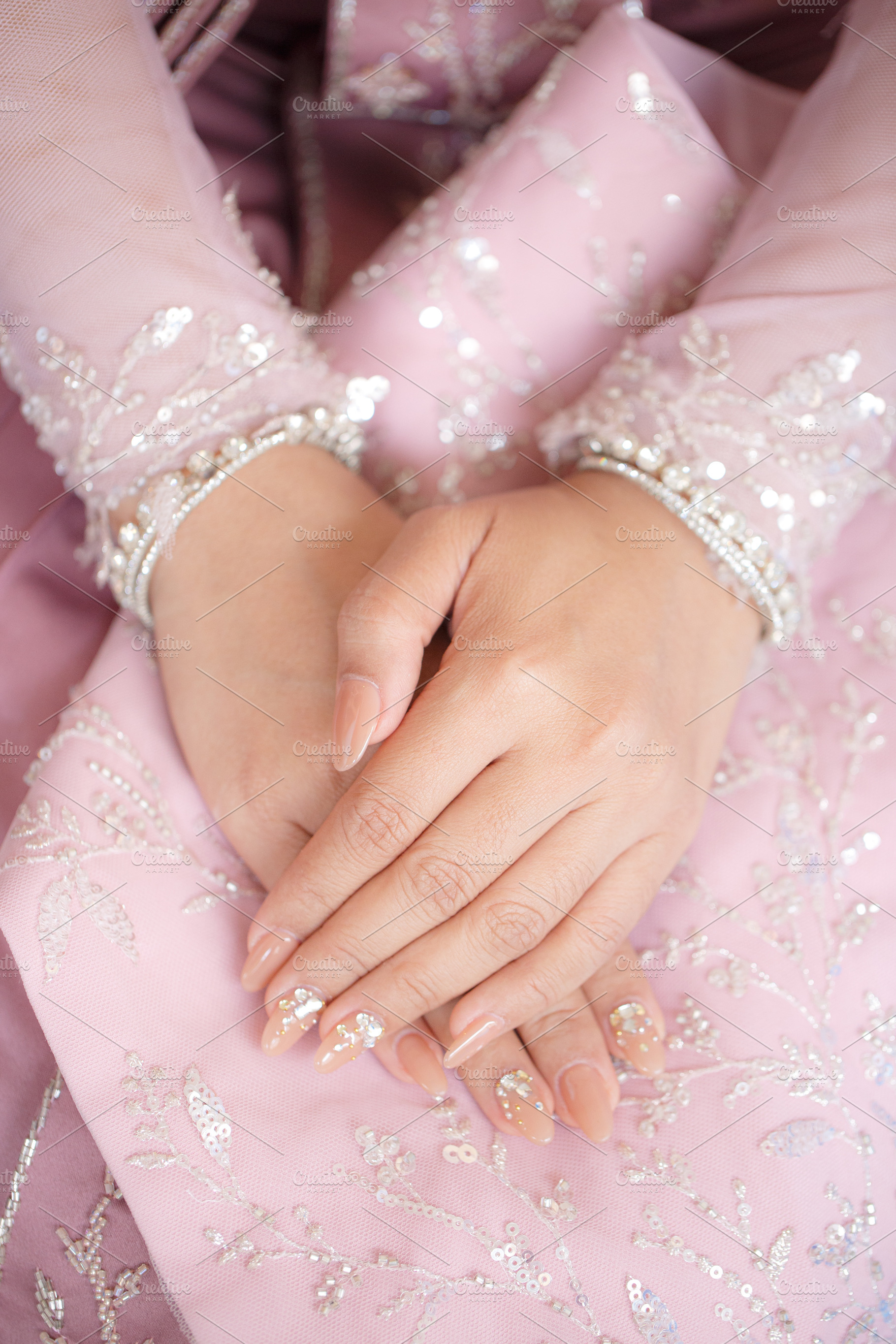 Elegant hands adorned with nail art resting on pink embroidered fabric, a Person Photo by a454
