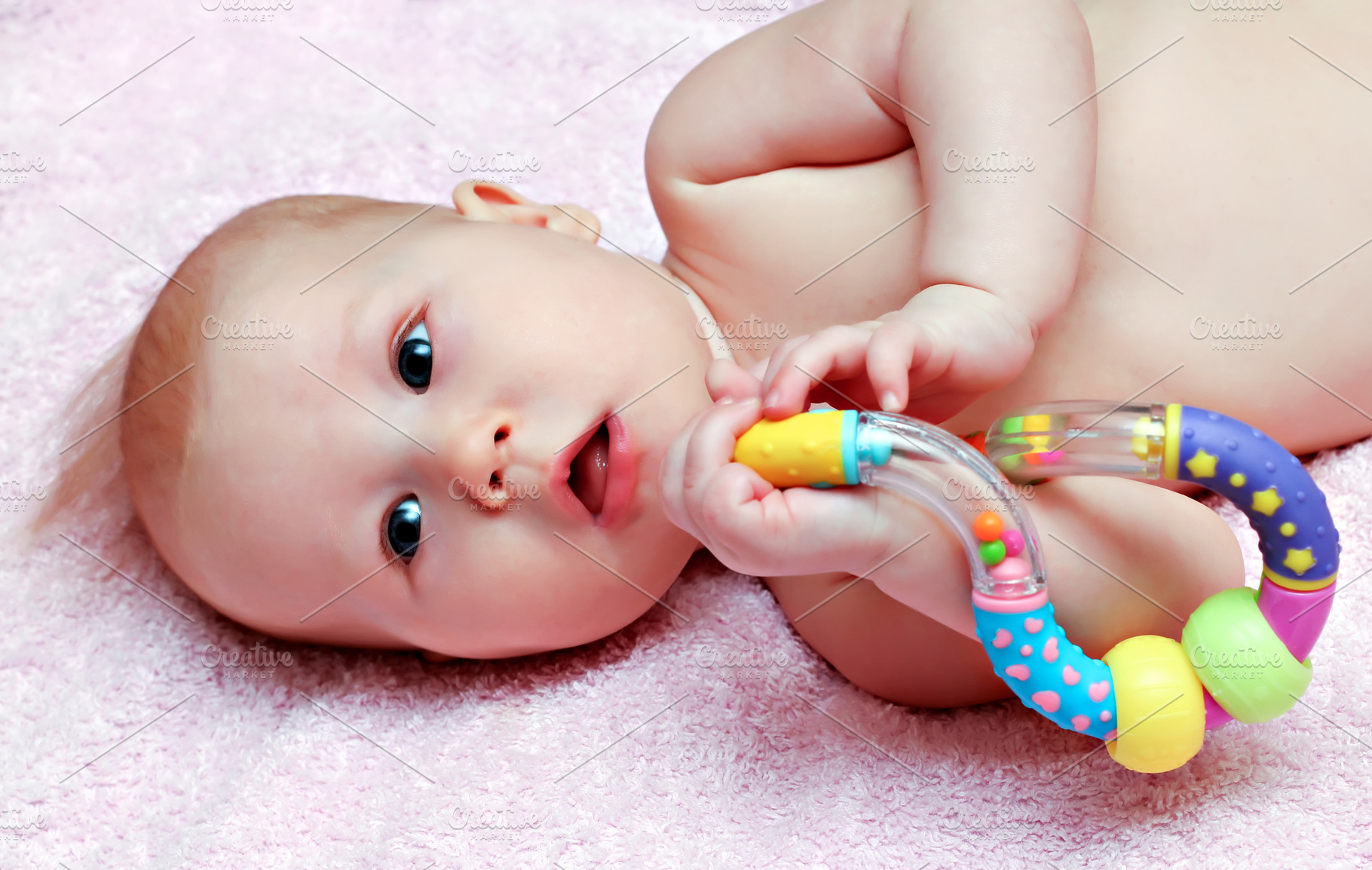 Newborn baby playing with colorful rattle, a Photo by saiko3p
