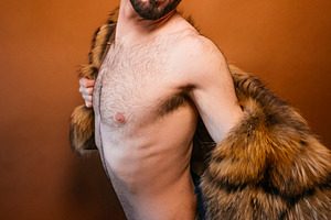 Confident man posing shirtless with fur coat and beanie, a Photo by karrastock