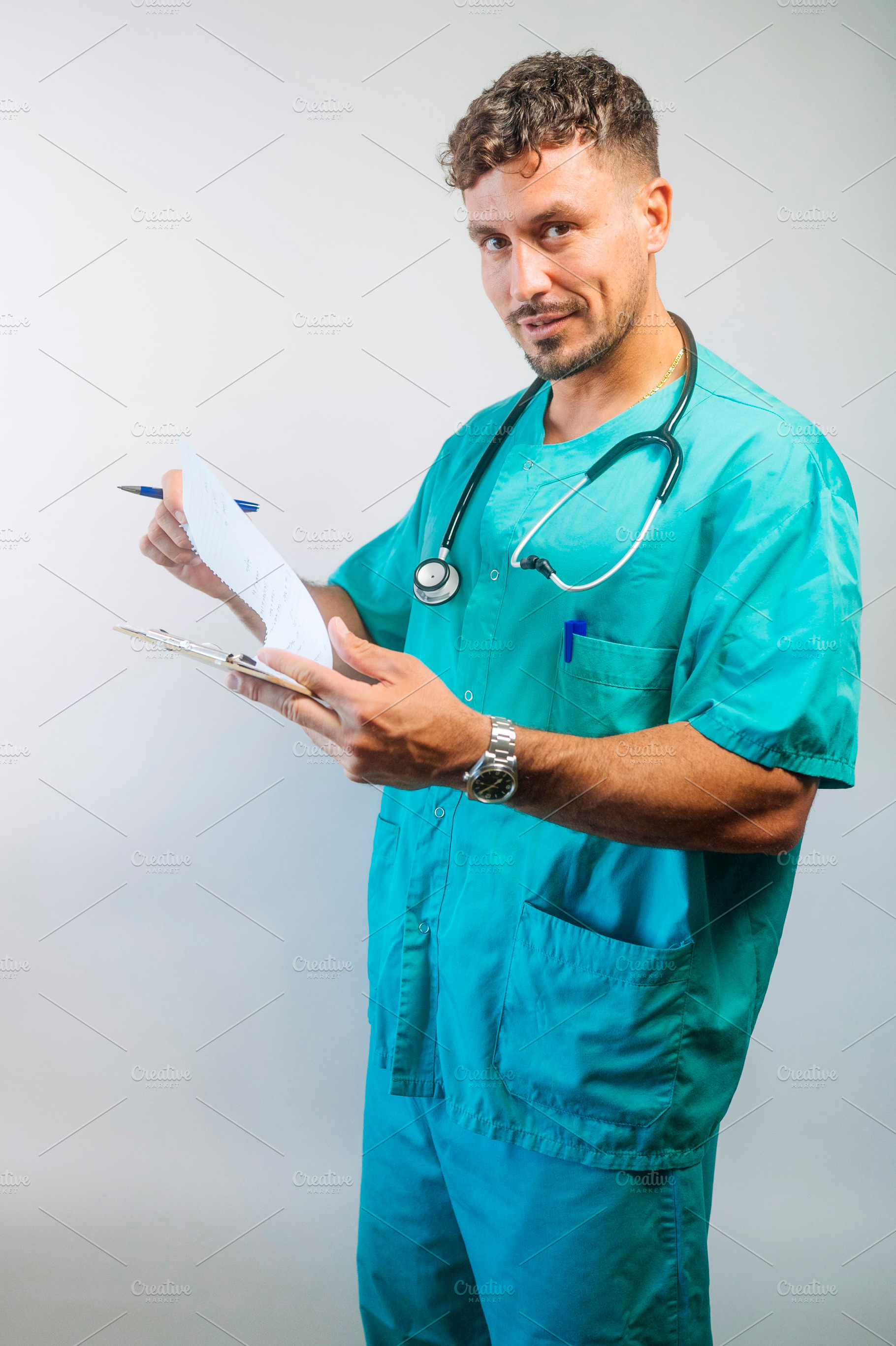 Focused male doctor reviewing documents on clipboard, wearing scrubs and stetho, a Person Photo by karrastock