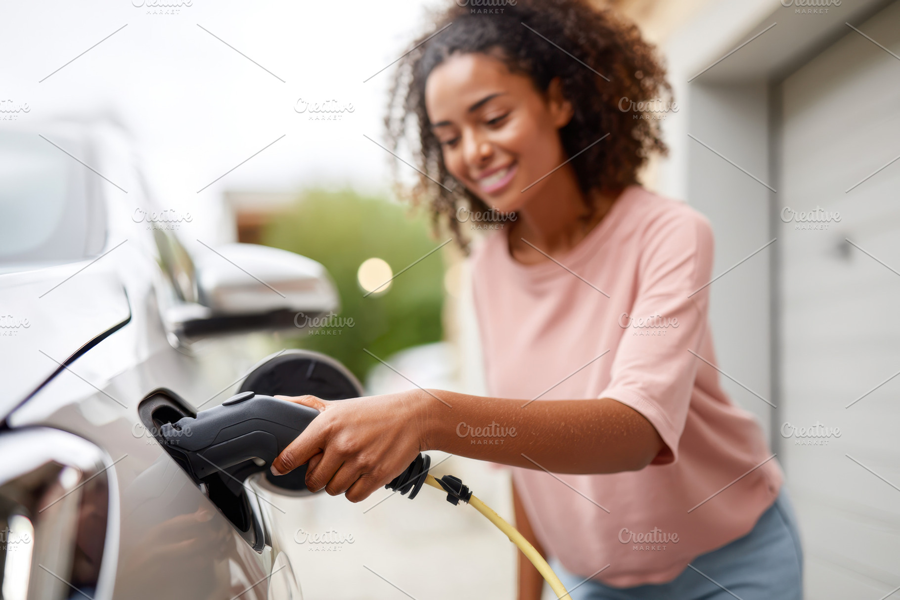 Woman charging electric vehicle at home, a Person Photo by AlyaAnd