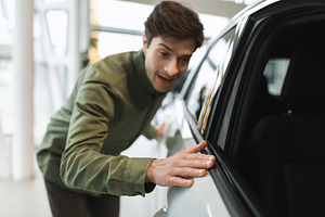 Happy young man touching new automobile of his dreams, buying modern car at dea, a Photo by Prostock-Studio