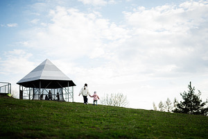Girl and child walking hand in hand toward a pavilion on a grassy hillside in a, a Person Photo by AS photostudio