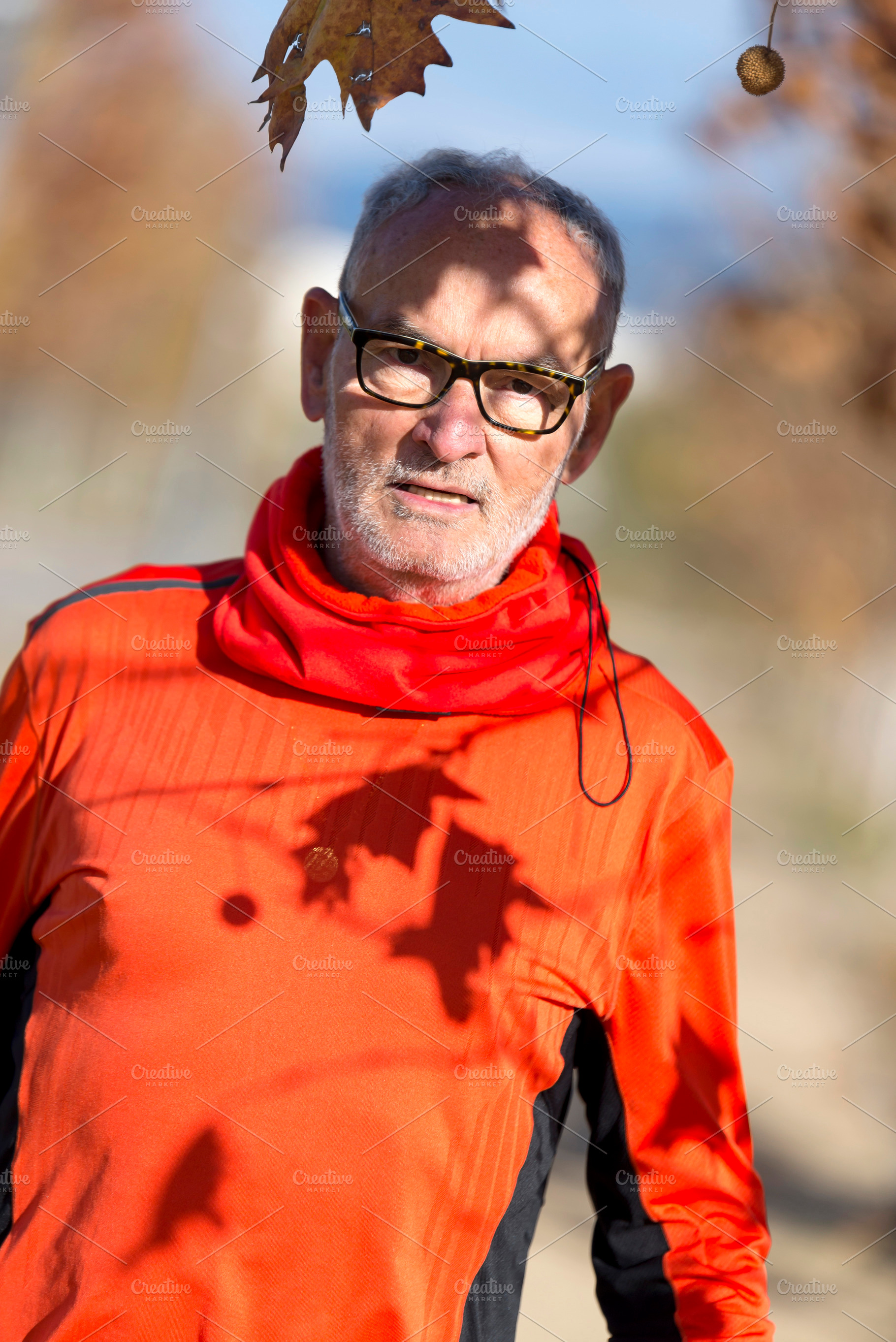 Senior man in red sportswear under autumn tree shadows, a Sports & Recreation Photo by RF Images