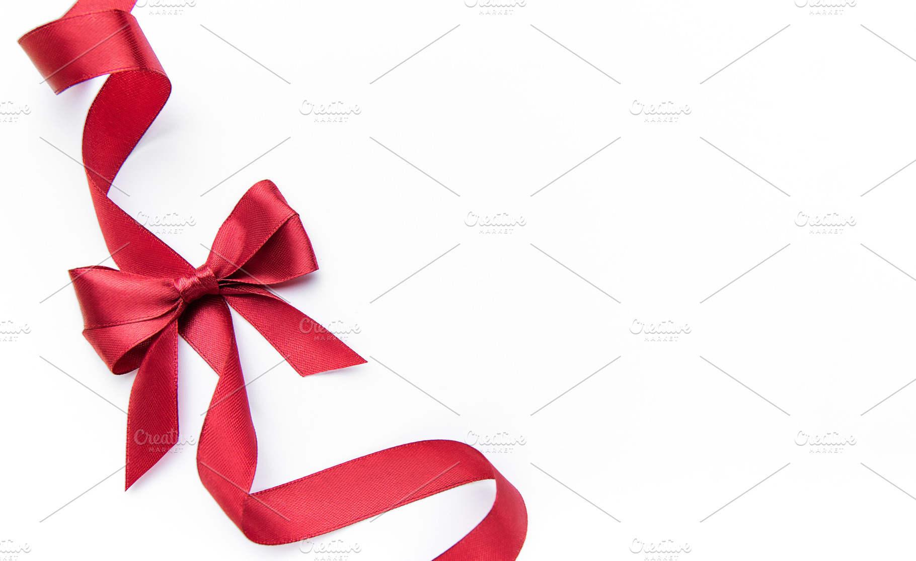 Red satin ribbon forming bow on white background, a Photo by Olena Rudo