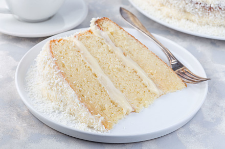 Piece of homemade coconut cake with cream cheese frosting and coconut flakes de, a Food & Drink Photo by iuliia_n