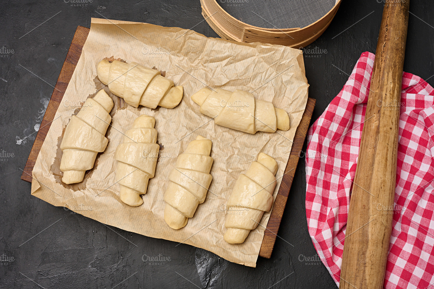 Uncooked croissant blanks on parchment paper and kitchen utensil, a Food & Drink Photo by ndanko