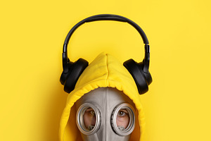Person in a yellow hoodie and gas mask wearing black headphones,, a Person Photo by Ales Munt