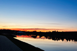 Serene sunset reflecting on a calm water canal with vibrant colors, a Photo by AS photostudio
