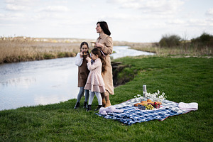 Mother and daughters enjoying a riverside picnic together on a blanket with foo, a Person Photo by AS photostudio