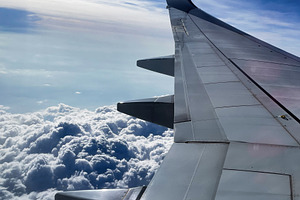 Airplane wing view over fluffy clouds with blue sky and sunlight, a Photo by AS photostudio