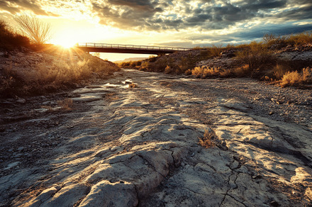 Sunset over dry riverbed with bridge, a Photo by Tanuart
