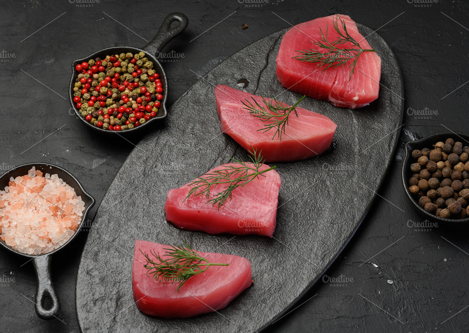 Raw tuna pieces on a black board, spices nearby, a Food & Drink Photo by ndanko