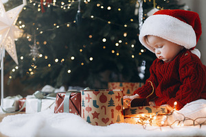 Adorable baby in santa hat opening stylish present boxes with ga, a Holiday Photo by Sonjachni