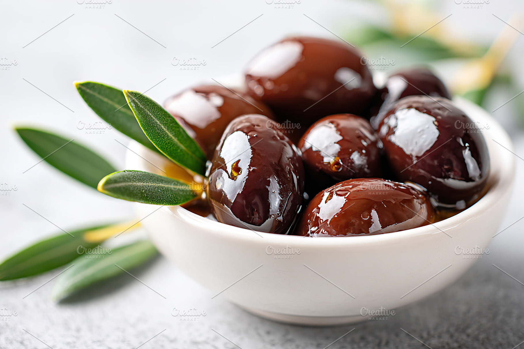 Glossy marinated olives served in a white bowl with olive leaves on a textured, a Food & Drink Photo by AlyaAnd