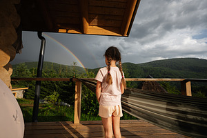 Girl standing on balcony with rainbow and mountain view in the background, a Photo by AS photostudio