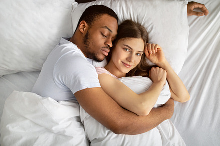 Young black guy sleeping and hugging his beautiful Caucasian girlfriend in bed,, a Photo by Prostock-Studio
