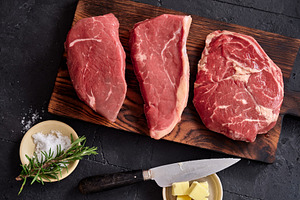 Raw rib-eye, roast beef, flank and rump steak on a wooden board with knife and, a Food & Drink Photo by Asya Nurullina