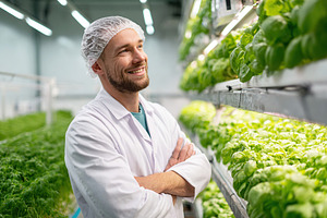 Worker smiles proudly in indoor herb farm surrounded by fresh basil plants, a Photo by AlyaAnd