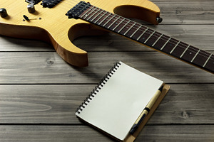 Guitar on wooden top & paper notepad featuring guitar, electric guitar, and