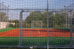Wide shot of an empty soccer field with red turf, green borders, and netted goa, a Sports & Recreation Photo by Ales Munt