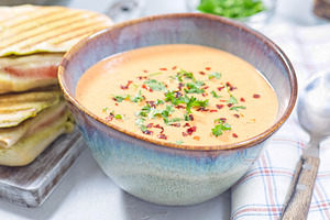 Bowl with Red bell pepper creamy soup served with grilled turkey panini, horizo
