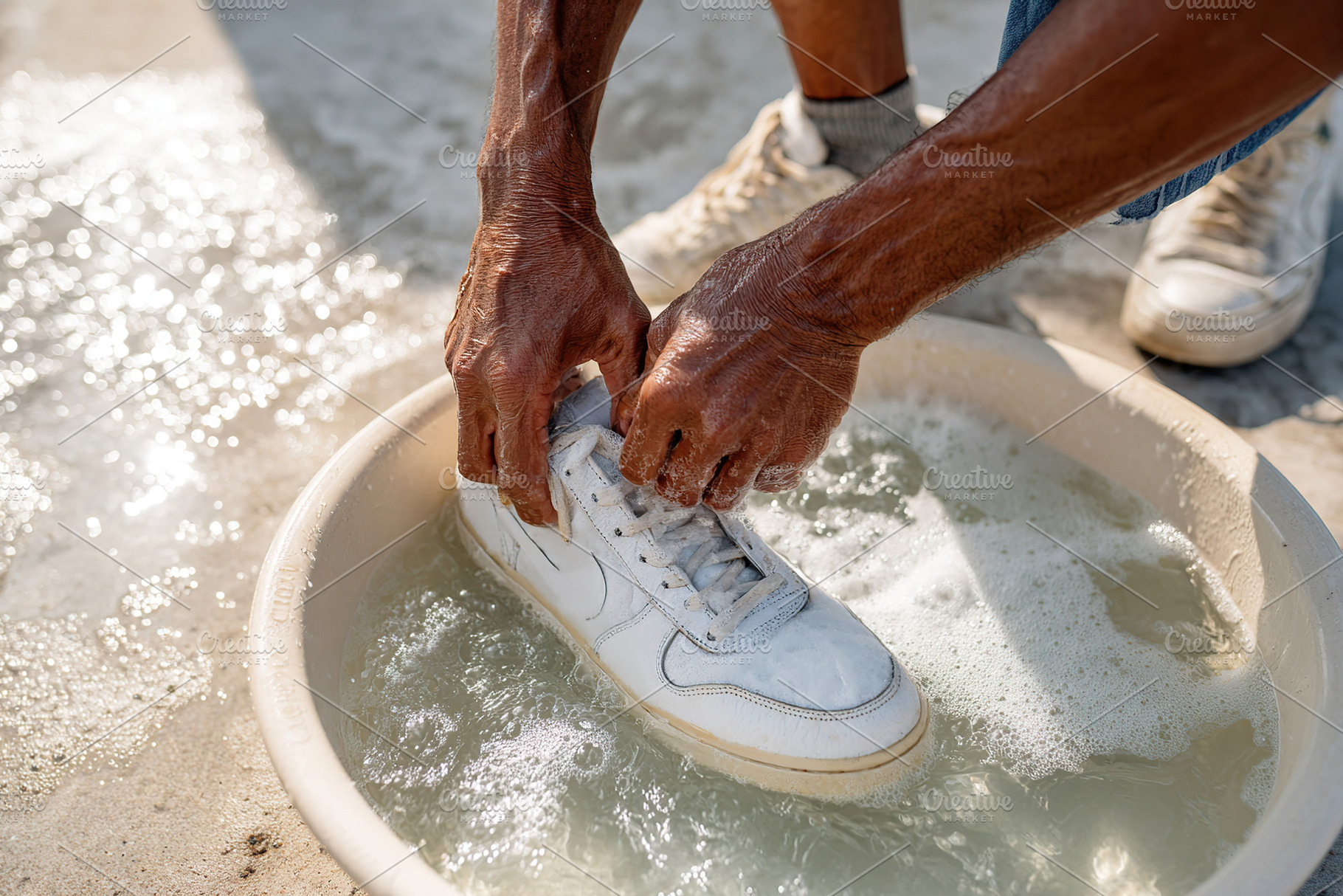Hands cleaning a white sneaker in a bowl of soapy water by the beach on a sunny, a Photo by AlyaAnd