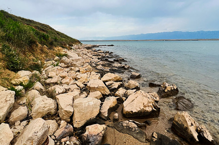 Rocky shoreline of a serene beach under cloudy sky, a Photo by AS photostudio