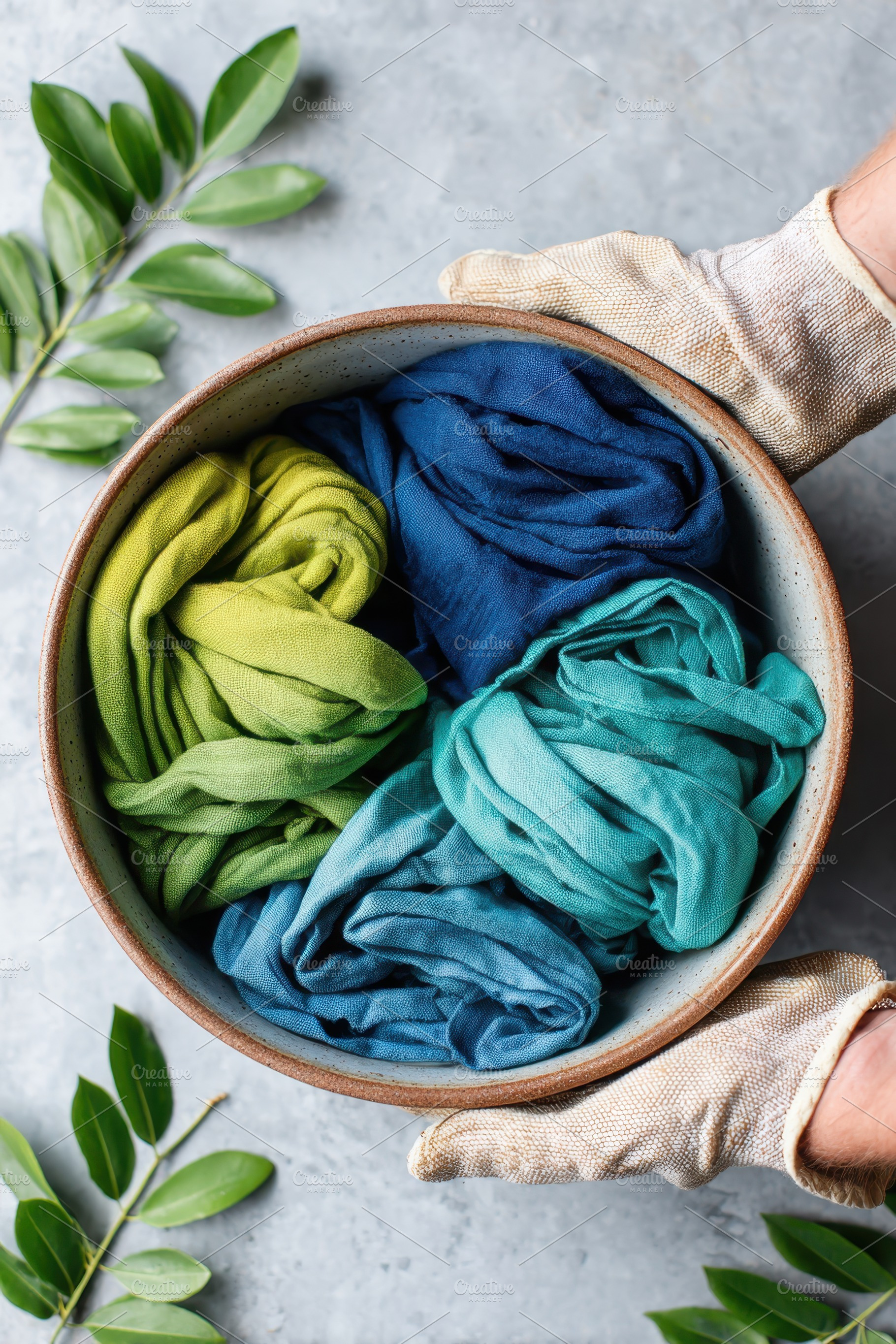 Colorful fabrics in a bowl with green leaves, an Abstract Photo by AlyaAnd