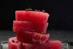 Stack of raw tuna pieces on black square plate, black background, a Food & Drink Photo by ndanko