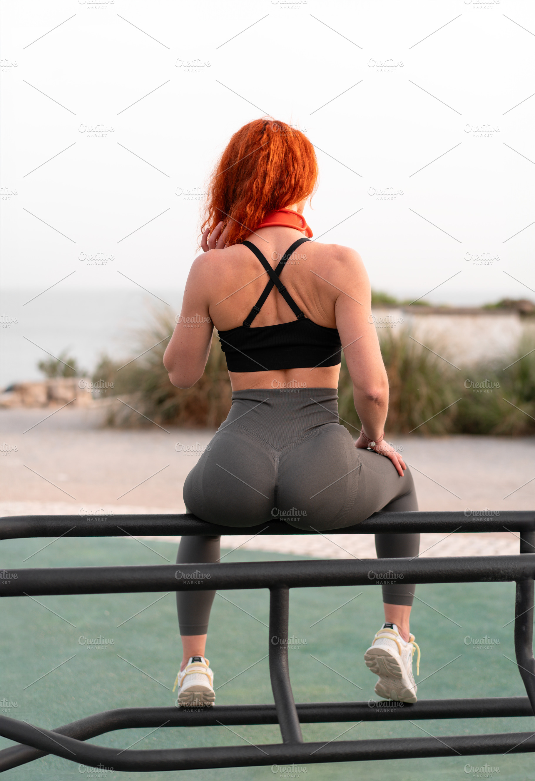 Sensuous jogger woman sitting on railing at beach during sunny day, a Person Photo by andreonegin market