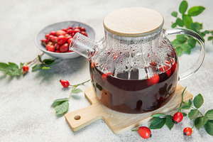 Steaming rosehip tea brewing in glass teapot on wooden board, a Food & Drink Photo by Olena Rudo