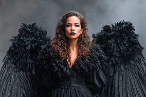 Model poses dramatically in black feathered wings against a smoky backdrop duri, a Photo by AlyaAnd
