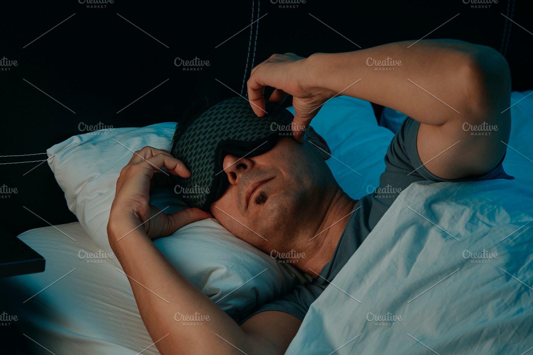 closeup of a man in bed adjusting his sleep mask, a Photo by Nito