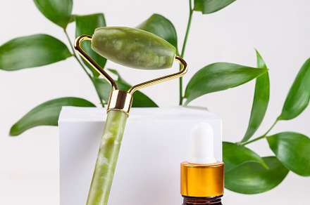 Jade crystal facial roller with brown cosmetic bottles and green leaves, home s, a Health & Medical Photo by iuliia_n