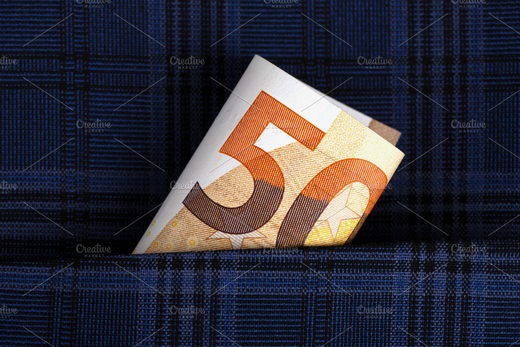 Close-up of a folded 50 euro banknote emerging from the pocket of a blue plaid, a Business Photo by Ales Munt