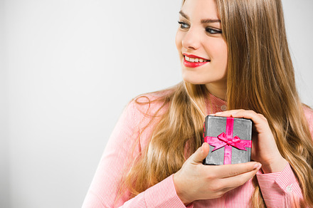 Portrait of a young happy blonde girl with long hair holding present in her hands