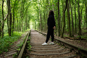 Woman standing on a railway surrounded by a lush green forest, a Photo by AS photostudio