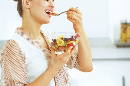 Happy young housewife eating fresh fruit salad in kitchen, a Food & Drink Photo by Alliance Images
