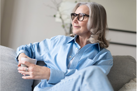 mature woman drinking coffee on sofa, a Person Photo by OPOLJA